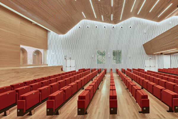 Interior view of the Congress Centre of Cordoba auditorium, featuring modern architectural design with wooden and white paneling, and rows of red seats; designed by LAP architects in Spain.